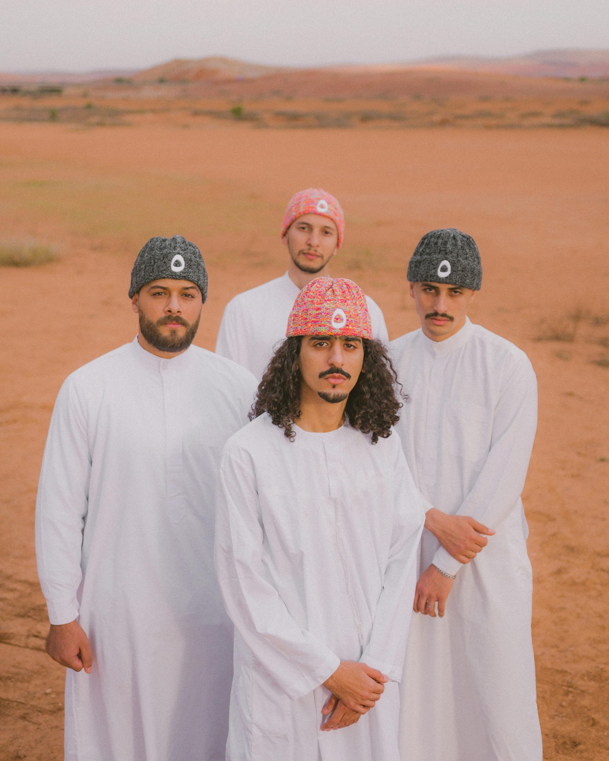 Four men in white traditional clothing stand in Morocco's desert landscape.